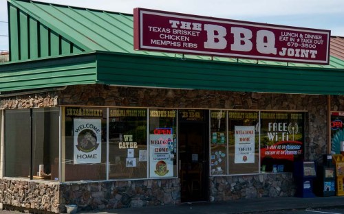 Exterior of a BBQ restaurant with a green roof, stone facade, and signs for Texas brisket, Memphis ribs, and free Wi-Fi.