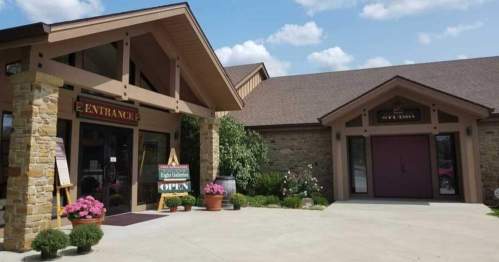 A welcoming entrance to a building with stone accents, potted plants, and a sign indicating it's open.