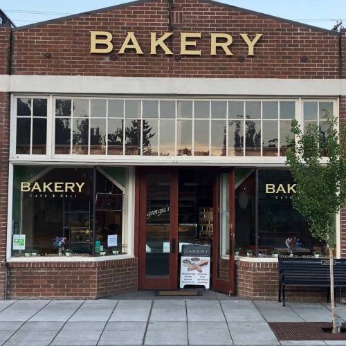A charming bakery storefront with large windows, displaying baked goods and a sign that reads "Bakery."