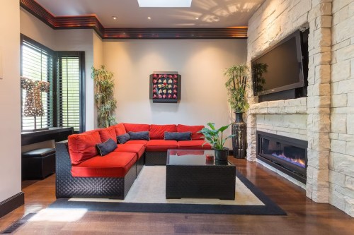 A modern living room featuring a red sectional sofa, stone fireplace, and decorative plants.