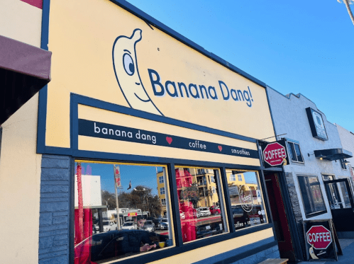 A colorful storefront with the sign "Banana Dang!" featuring a cartoon banana, promoting coffee and smoothies.