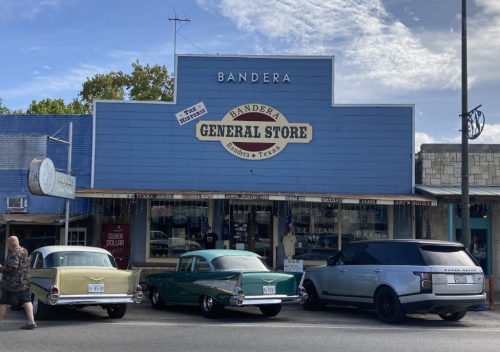 A blue general store in Bandera, Texas, with vintage cars parked outside and a person walking by.