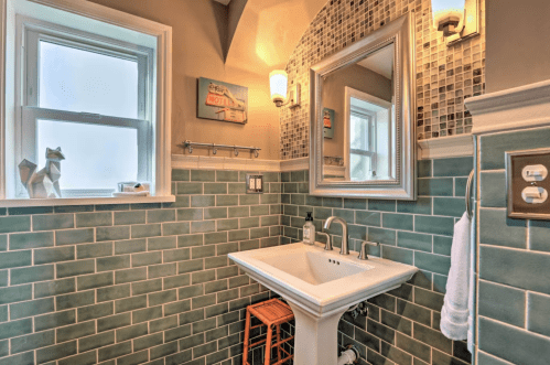 A stylish bathroom featuring green tiled walls, a modern sink, a mirror, and a window with natural light.