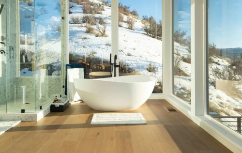 Modern bathroom featuring a freestanding tub, large windows with snowy landscape views, and a glass shower.