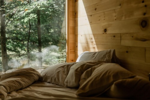 Cozy bed with soft pillows, bathed in natural light from a large window overlooking a serene forest.