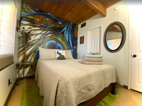 Cozy bedroom featuring a peacock feather mural, a neatly made bed, and decorative towels on a green rug.