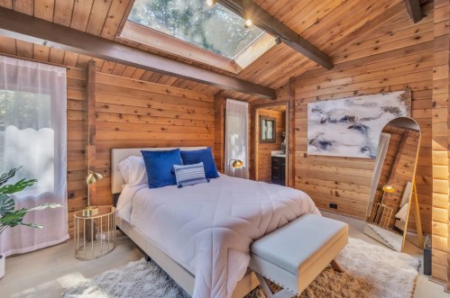 Cozy wooden bedroom with a skylight, white bedding, blue accents, and a stylish rug.