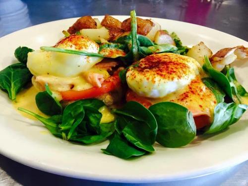 A plate of eggs Benedict with spinach, tomatoes, and potatoes, garnished with paprika.