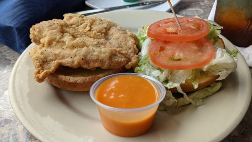 A plate with a fried chicken sandwich, lettuce, tomato, and a side of dipping sauce.