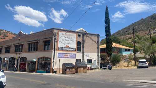 A street view of a historic building with a large sign, surrounded by trees and mountains under a blue sky.