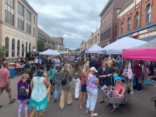 A bustling street market with tents, vendors, and crowds of people shopping and socializing on a cloudy day.