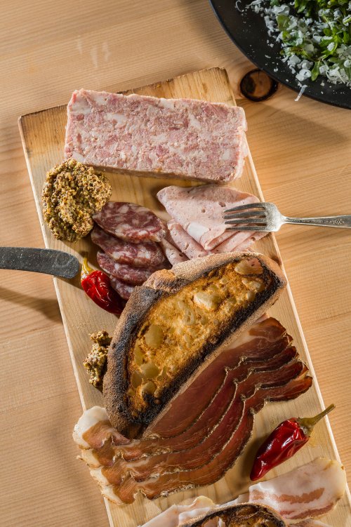 A wooden platter featuring assorted meats, pâté, mustard, and toasted bread, garnished with red peppers.