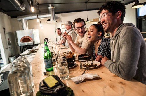A group of friends enjoying a meal at a bar, laughing and sharing dishes in a cozy restaurant setting.