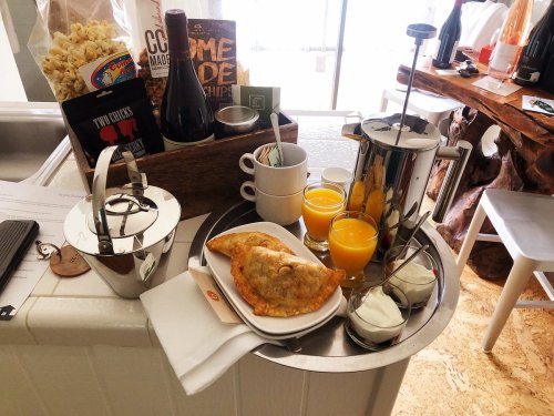 A tray with a coffee pot, orange juice, pastries, popcorn, and a bottle of wine, set in a cozy kitchen.