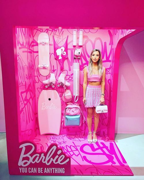A display featuring a Barbie-themed setup with pink accessories, a skateboard, and a model in a matching outfit.