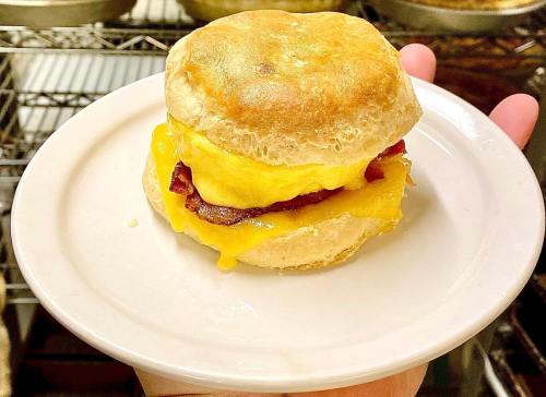 A golden biscuit sandwich with melted cheese, bacon, and scrambled eggs on a white plate.