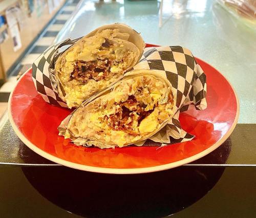 A close-up of a plate with two halved burritos wrapped in paper, showcasing a filling of eggs and meat.
