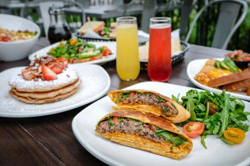 A table set with various dishes, including tacos, pancakes topped with strawberries, and colorful drinks.