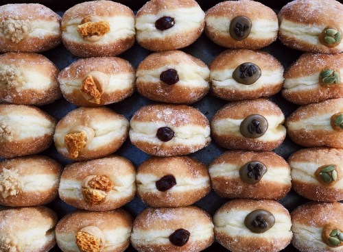 A tray of assorted doughnuts filled with cream, topped with various flavors and textures.