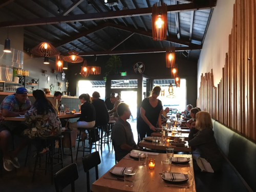 A cozy restaurant interior with diners at tables, warm lighting, and a server attending to guests.
