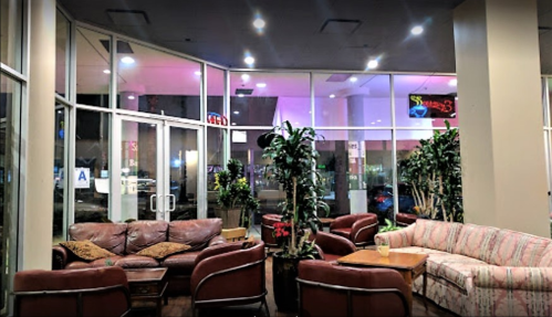 Cozy lounge area with leather sofas, plants, and large windows, illuminated by soft lighting and neon signs.