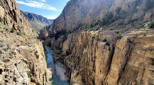 A scenic view of a deep canyon with steep rock walls and a winding river at the bottom under a clear blue sky.