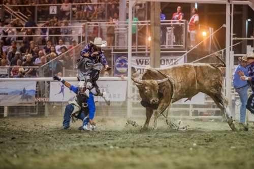 A cowboy attempts to ride a bucking bull while another cowboy braces for impact in a rodeo arena.