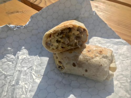 A close-up of a burrito cut in half, revealing a filling of meat and cheese, resting on a patterned paper.