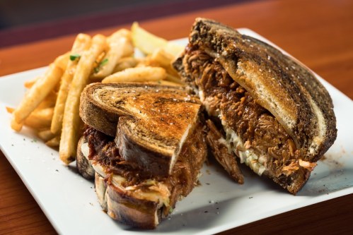 A close-up of a pulled pork sandwich on toasted bread, served with a side of crispy French fries.