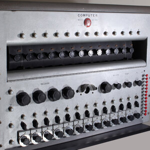 A vintage computer with numerous knobs and switches, featuring a metallic finish and labeled controls.
