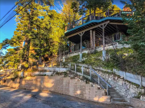 A hillside home with a deck, surrounded by trees and a stone pathway leading up from the road.