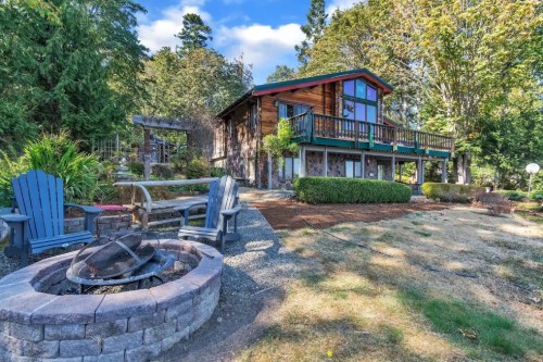 A charming wooden house with a balcony, surrounded by greenery and a fire pit in the foreground.