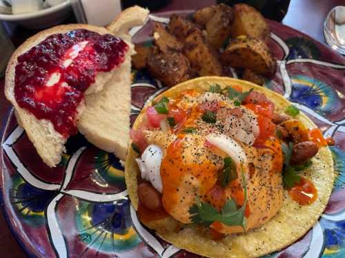 A colorful plate featuring a taco with beans, tomatoes, and sauce, alongside a slice of bread with jelly and roasted potatoes.