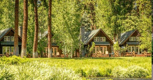 A serene landscape featuring three cozy cabins surrounded by lush greenery and tall trees.