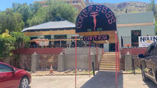 Sign for Contessa's Cantina with a red awning, surrounded by greenery and a building in the background.