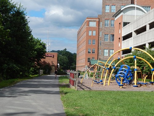 A pathway beside a playground with colorful equipment and a building in the background under a partly cloudy sky.