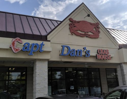 Signage of Capt Dan's Crab House, featuring a crab logo, with a blue sky and clouds in the background.
