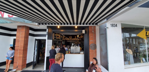 A coffee shop entrance with striped awning, people inside and outside, and a sign reading "Captain's Grounds."