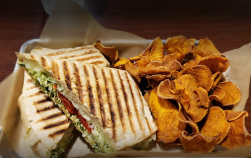 A grilled sandwich with vegetables and a side of crispy sweet potato chips on a tray.