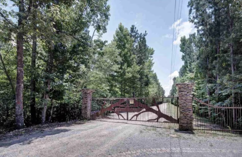 A gated entrance surrounded by tall trees and a gravel road leading into a wooded area.