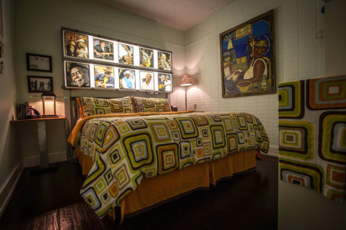 Cozy bedroom featuring a patterned bedspread, framed artwork, and warm lighting.
