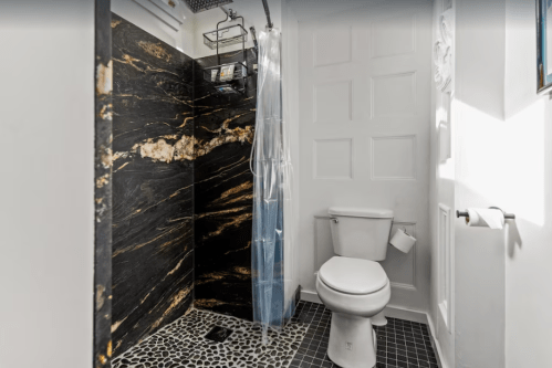 A modern bathroom featuring a black marble shower, a clear curtain, and a white toilet on a patterned floor.