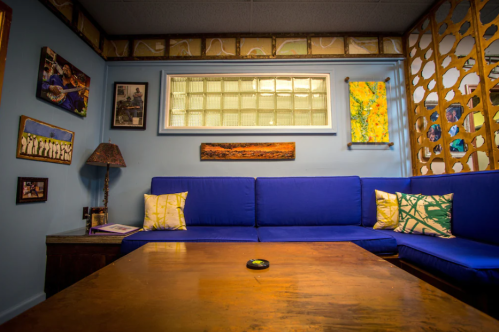 Cozy room with blue couches, a wooden table, and colorful artwork on the walls. Warm, inviting atmosphere.