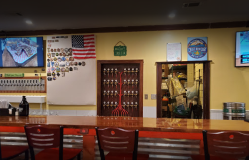 A bar interior featuring a wooden counter, beer taps, wall decor, and screens displaying images.