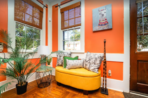 Cozy corner with an orange wall, yellow bench, decorative pillows, a lamp, and a giraffe statue.