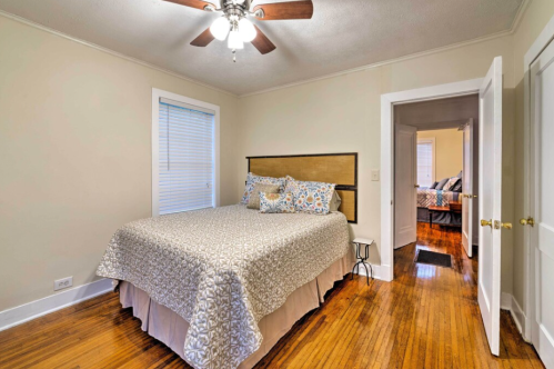 Cozy bedroom with a queen bed, decorative bedding, a ceiling fan, and a doorway leading to another room.