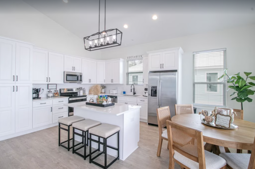 Modern kitchen with white cabinets, stainless steel appliances, a central island, and a dining table with wooden chairs.