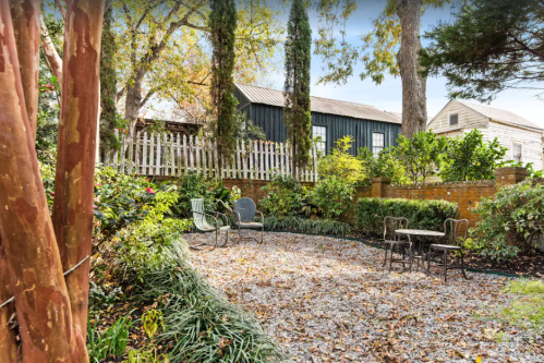 A serene garden with gravel paths, surrounded by greenery, featuring two chairs and a small table.