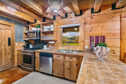 Cozy wooden kitchen with stainless steel appliances, open shelving, and a scenic window view.