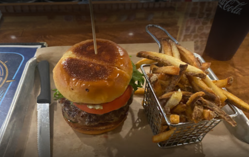 A juicy burger with lettuce and tomato, served with a side of crispy fries in a small basket.